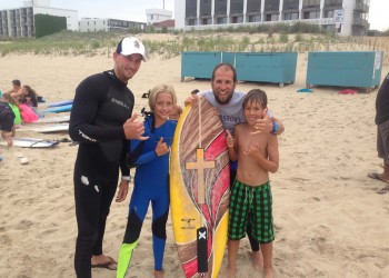 group of four posing for picture behind surfboard
