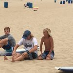 Three young boys sitting on the beach at Surf School