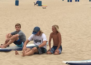 Three young boys sitting on the beach at Surf School