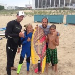 group of four posing for picture behind surfboard